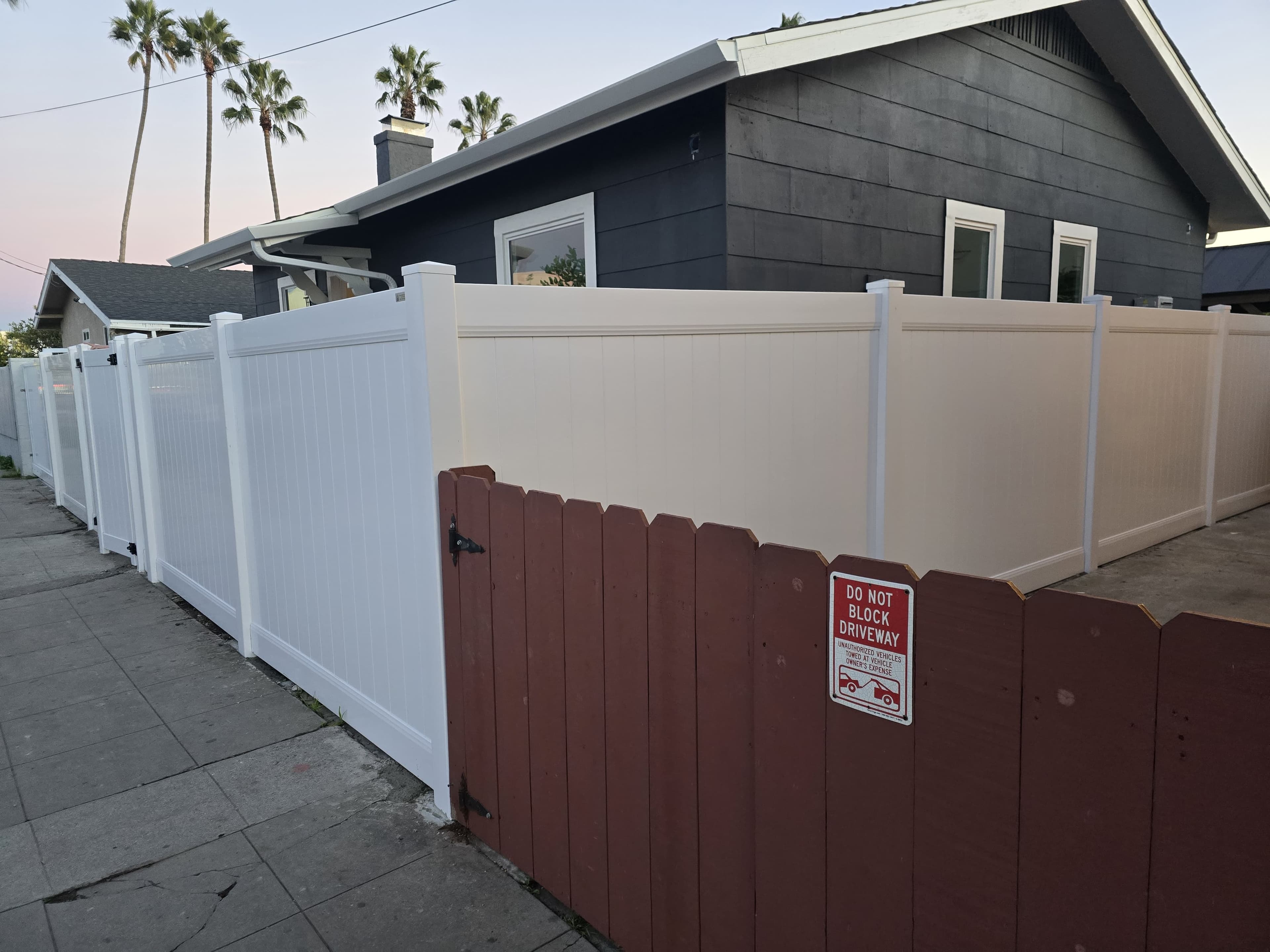 White vinyl privacy fence along a residential sidewalk with gate sections